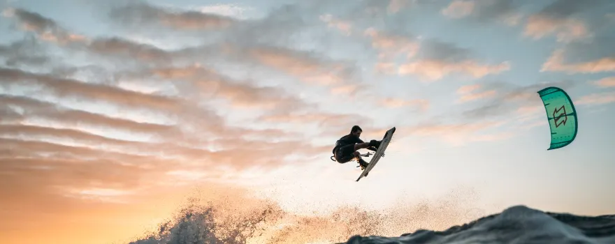 A kiteboarder airborne against a pale sunset over the bay